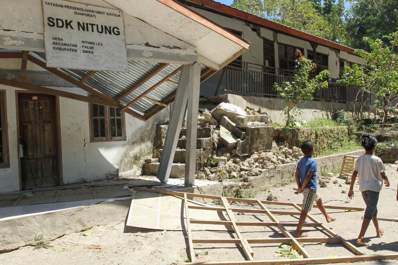 Children walk past a damaged school on Aug. 19 in Sukka regency, East Nusa Tenggara (NTT). A 7.7-magnitude earthquake off the northern coast of Flores Island damaged hundreds of homes and other buildings in the region.
