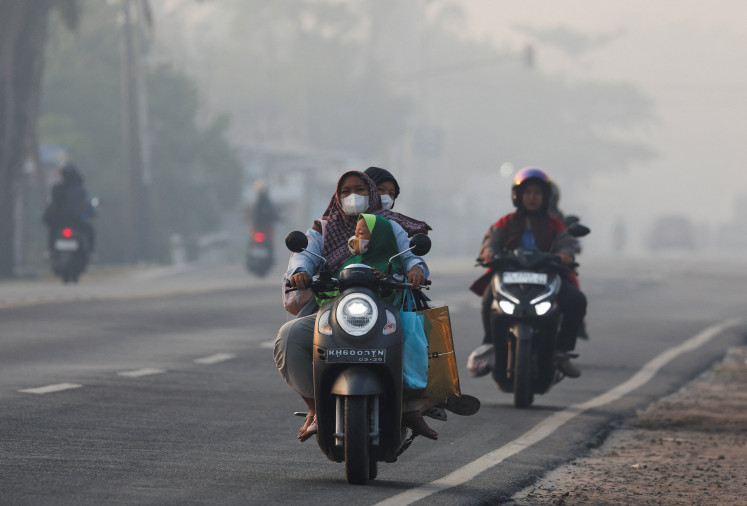 Riders wear protective masks as smog covers the area due to recent wildfires in Palangka Raya, Central Kalimantan on August 14, 2026.