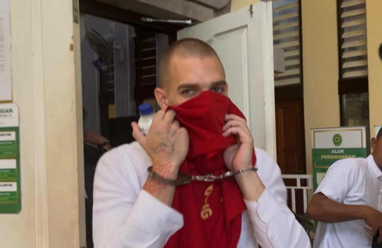 Luzian Andrin Zgraggen, 26, covers his face on Aug. 20, 2026, as he departs his verdict and sentence hearing at the Denpasar District Court in the Bali capital, which found the Swiss national guilty of spreading hate speech over Nyepi (Day of Silence) in March.