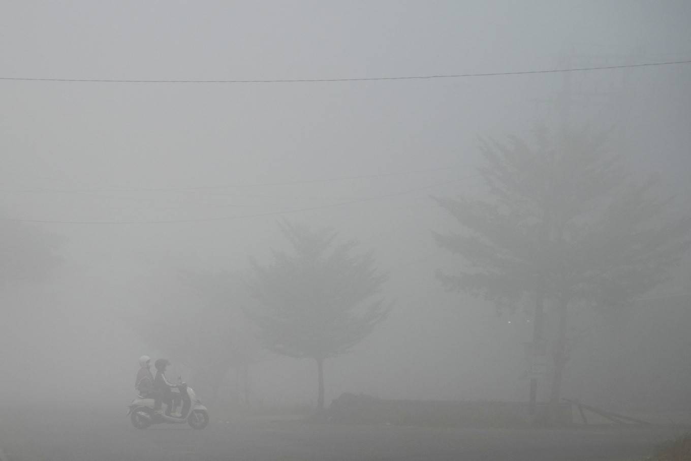 A motorcyclist and a passenger pass along a road shrouded in haze caused by wildfires on Aug. 23, 2026, in Banyuasin regency, South Sumatra.