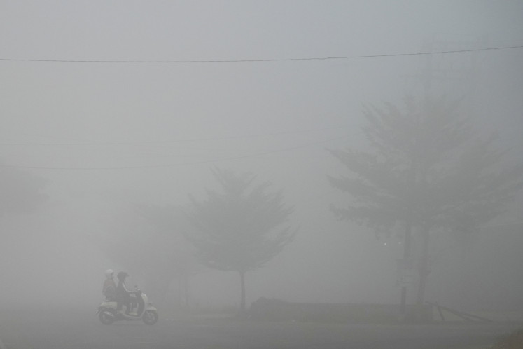 A motorcyclist and a passenger pass along a road shrouded in haze caused by wildfires on Aug. 23, 2026, in Banyuasin regency, South Sumatra.