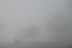 A motorcyclist and a passenger pass along a road shrouded in haze caused by wildfires on Aug. 23, 2026, in Banyuasin regency, South Sumatra.