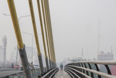Residents wear masks as they cross Siak IV Bridge, shrouded in haze on Aug. 24 in Pekanbaru, Riau. The Riau provincial administration has urged residents to reduce outdoor activities and wear protective masks while outdoors as air quality in Pekanbaru deteriorates due to smoke from forest and land fires.
