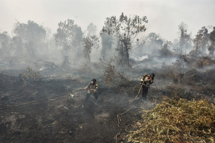 Police in firefighting gear extinguish a peatland fire at Tambang in Kampar, Riau province, on August 25, 2026.