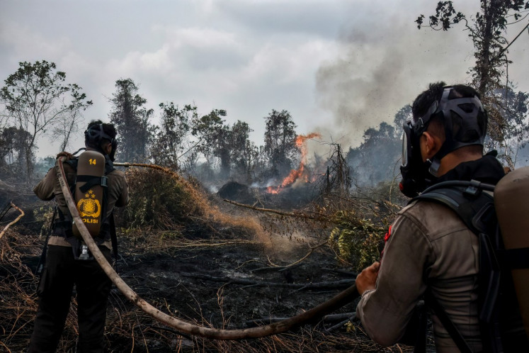 Police in firefighting gear extinguish a peatland fire at Tambang in Kampar, Riau, on Aug. 25, 2026. 