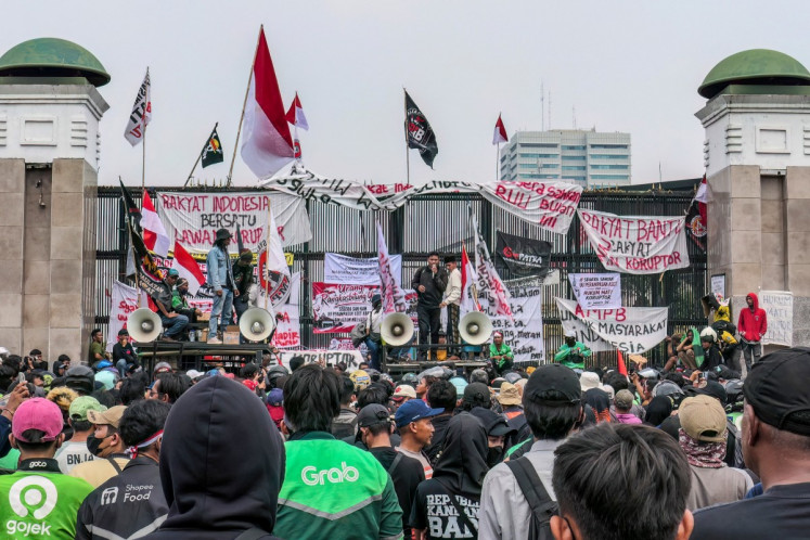 Protesters deliver speeches and put up posters and banners on a gate on Thursday during a demonstration urging lawmakers to immediately pass an asset forfeiture law for corruptors outside the Legislative complex in Jakarta.