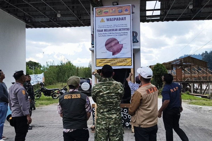 Officials from various agencies look on as two men install a poster warning residents and tourists not to approach Mount Sinabung on Aug. 29 in Karo regency, North Sumatra. The Mount Sinabung Monitoring Post has increased the volcano's status to Level II Waspada (advisory) following increased volcanic activities.