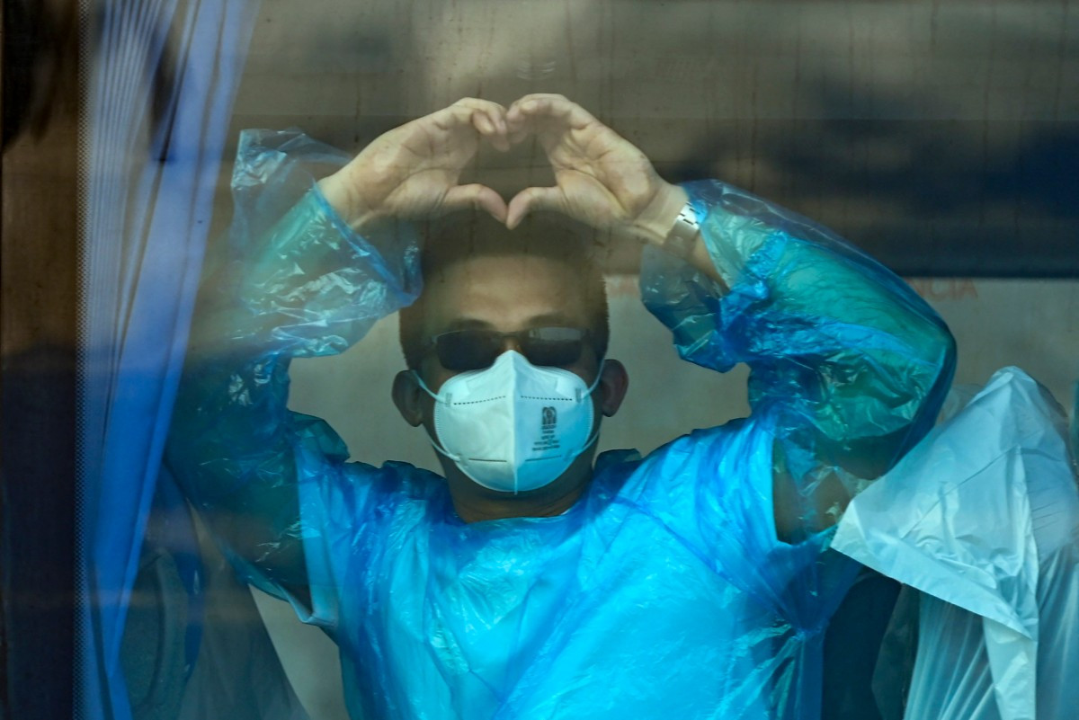 A passenger of the hantavirus-stricken cruise ship MV Hondius makes the heart hands sign on May 11, 2026, as he leaves aboard a military bus from the port of Granadilla de Abona on Tenerife in the Canary Islands, Spain.