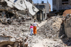 Two girls walk past the rubble of collapsed buildings on Aug. 25 in Khan Yunis in the southern Gaza Strip. A ceasefire in October 2025 has reduced but not halted the violence in Gaza. Israeli operations have killed 1,288 people since the ceasefire came into effect, according to Gaza's health ministry, which also operates under Hamas authority and whose figures are considered reliable by the United Nations.