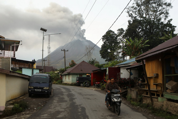 A motorcyclist rides through Kutarayat village, Karo, North Sumatra, as Mount&nbsp;Sinabung&nbsp;volcano erupts in the background on Sept. 2, 2026. 