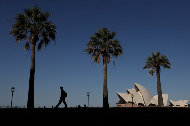 A man walks through a park with the Sydney Opera House in the background on the first day of spring in Sydney, Australia, on Sept. 1, 2026.