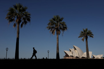 A man walks through a park with the Sydney Opera House in the background on the first day of spring in Sydney, Australia, on Sept. 1, 2026.