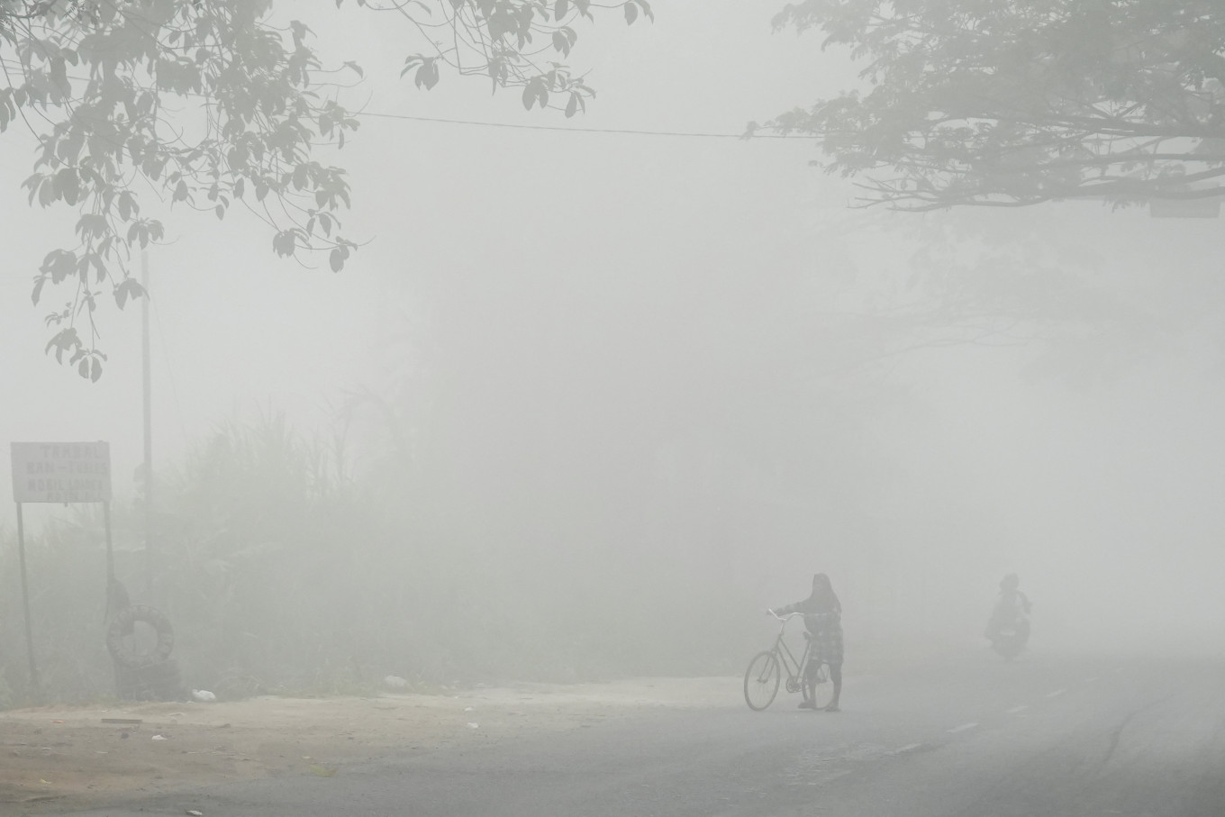 A person walks with a bicycle along a road shrouded in haze from wildfires in Banyuasin, South Sumatra, September 6, 2026. 