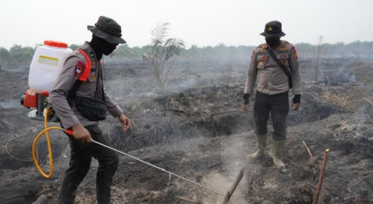 A noncommissioned police officer (left) sprays the X Fire solution over a peatland area on Friday while an officer observes the spraying in Sering village, Pangkalan Kerinci district in Pelalawan regency, Riau. Made by the National Police's Logistics Staff and the Mobile Brigade (Brimob), the solution is made from a mixture of crude palm oil (CPO) and tapioca flour and is expected to contain forest fires by cutting oxygen supply.  