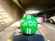 Industry helm: An online motorcycle taxi driver, wearing a helmet with the instantly recognizable logo of Singaporean super app Grab, drives through an underpass on July 27, 2026 in Kuningan, South Jakarta.