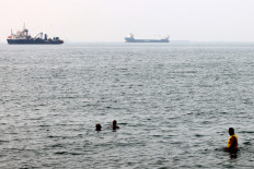 Men bathe in the Gulf waters as vessels in the background transit the Strait of Hormuz off the coast of Iran's southern port city of Bandar Abbas on Sept. 7, 2026.