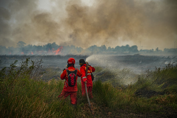 Firefighters from the specialized peatland wildfire tactical unit (Manggala Agni) direct a high-pressure water stream at a burning area in a field of tall dry grass in Ogan Ilir, South Sumatra on Sept. 25, 2026. Low visibility caused by persistent forest fires has hampered both commercial air travel and aerial firefighting operations across the province.