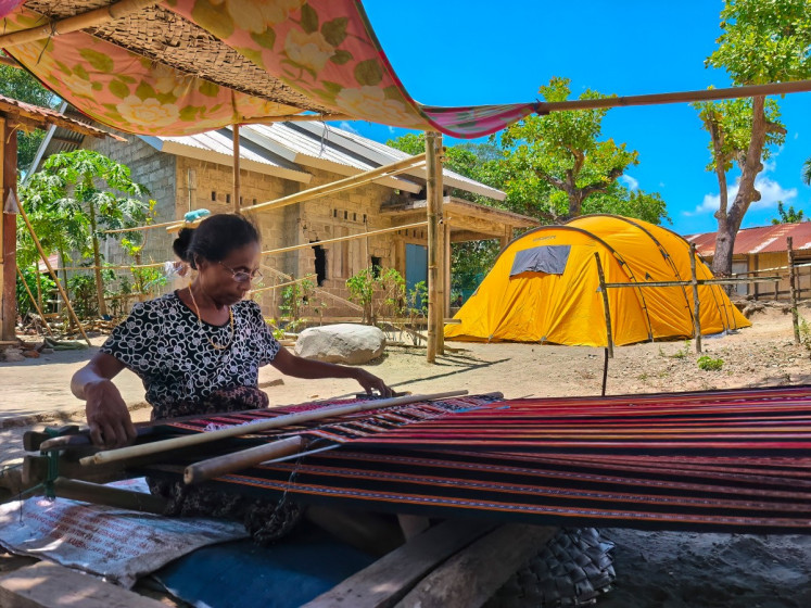 This picture taken on August 14, 2026 shows a woman weaving outside her home after it was damaged at Meken Detun village, Sikka regency, East Nusa Tenggara (NTT), following a 7.7-magnitude earthquake on August 15. The quake near Flores island damaged tens of thousands of homes and left the water supply in limbo on one small island, but it has also been followed by roughly 15,000 aftershocks. 