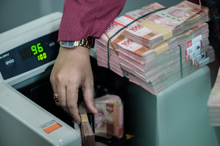 A teller places a bundle of Rp 100,000 banknotes in a money counting machine on June 4, 2026, at a currency exchange office in Jakarta.
