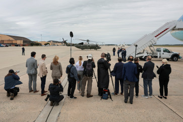 A reporter from Real America's Voice News, after the White House has blocked CNN from traveling with President Donald Trump on Air Force One for a trip on Saturday to Tennessee, and other media members stand next to Air Force One with a US military transport helicopter seen in the background at Joint Base Andrews, Maryland, US, September 26, 2026.