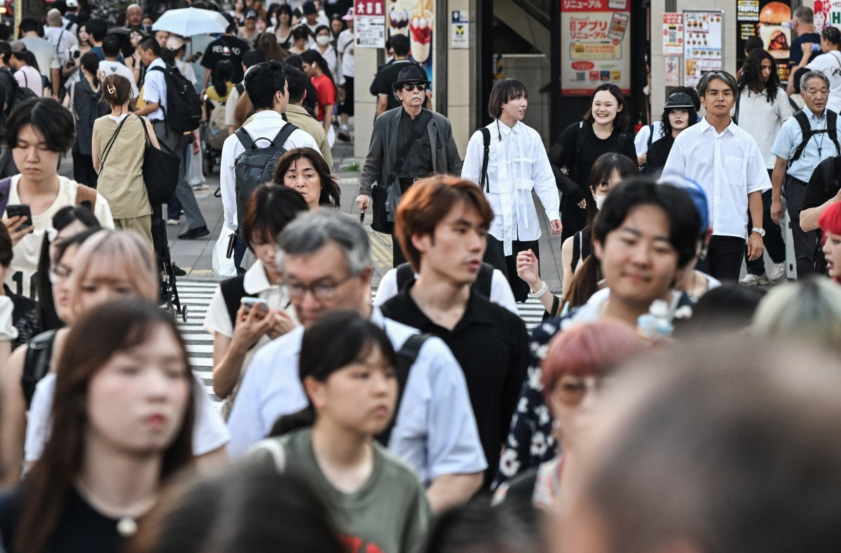 Tourists and commuters cross an intersection near shops in Shinjuku in Tokyo on July 21, 2026.