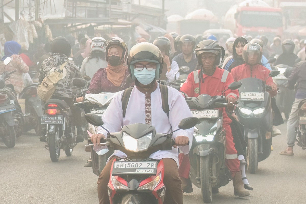 Motorcyclists commute on Oct. 2, 2026, as haze from forest and land fires shroud the road, in Palembang, South Sumatra. Wildfires in Indonesia have been blamed in large part on slash-and-burn land-clearing practices that result in the destruction of fire-resistant forest cover and the draining of peatlands.