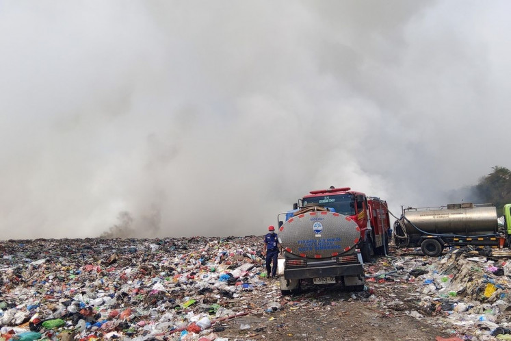 A Semarang city firefighter walks next to two water tankers and a fire truck on Thursday at Jatibarang landfill in Semarang. The fire started on Wednesday and affects some 10 hectares of the 46.18-ha landfill. 