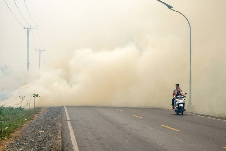 A couple rides a motorcycle through thick haze from forest and land fires in Barito Kuala, South Kalimantan, on October 10, 2026. Toxic haze has shrouded parts of Indonesia, Malaysia and Singapore for weeks as Jakarta struggles to contain fires that have scorched large tracts of Kalimantan and Sumatra, with the smoke drifting across the region.