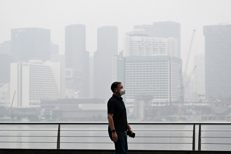 A pedestrian wearing a mask walks along the boulevard at Marina bay as buildings are seen shrouded with haze in Singapore on October 12, 2026. Indonesia has been battling fires for weeks in parts of Borneo and Sumatra, sending suffocating haze across the islands and neighboring Malaysia and Singapore.
