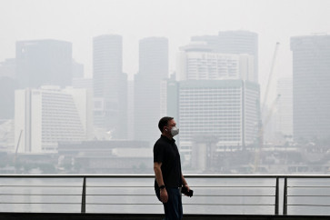 A pedestrian wearing a mask walks along the boulevard at Marina bay as buildings are seen shrouded with haze in Singapore on October 12, 2026. Indonesia has been battling fires for weeks in parts of Borneo and Sumatra, sending suffocating haze across the islands and neighboring Malaysia and Singapore.