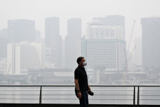 A pedestrian wearing a mask walks along the boulevard at Marina bay as buildings are seen shrouded with haze in Singapore on October 12, 2026. Indonesia has been battling fires for weeks in parts of Borneo and Sumatra, sending suffocating haze across the islands and neighboring Malaysia and Singapore.