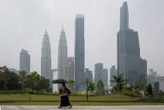 A woman walks as haze shrouds Petronas Twin Towers and other commercial buildings in Kuala Lumpur, Malaysia, on Oct. 13, 2026. Toxic haze has shrouded parts of Indonesia, Malaysia and Singapore for weeks as Indonesian authorities struggle to contain fires that have scorched large tracts of Kalimantan and Sumatra, with the smoke drifting across the region.