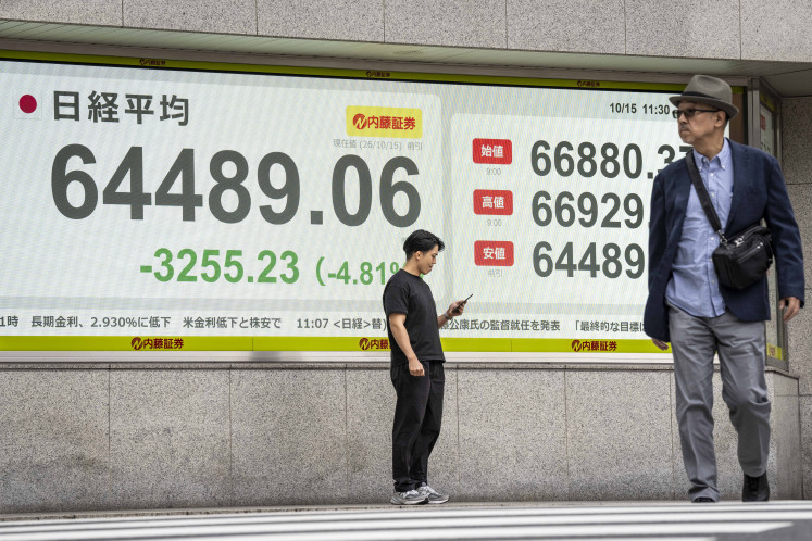 A man checks his phone in front of an electronic quotation board displaying the Nikkei Stock Average on the Tokyo Stock Exchange in Tokyo on Oct. 15, 2026.