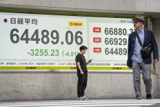 A man checks his phone in front of an electronic quotation board displaying the Nikkei Stock Average on the Tokyo Stock Exchange in Tokyo on Oct. 15, 2026.