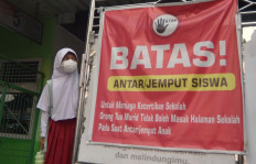 Murky schooling: A schoolgirl waits to be picked up on Sept. 16, 2026 next to a sign on drop-off/pickup rules at a school in Padang, after classes were let out early as West Sumatra&rsquo;s provincial capital reinstated remote learning in response to a spike in the air pollutant standards index (ISPU) to 900 due to dense haze.