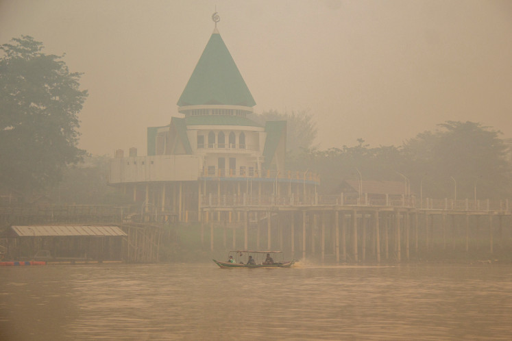 People ride a wooden boat on the Kahayan River as haze from wildfires shrouds Palangka Raya in Central Kalimantan, on October 18, 2026.