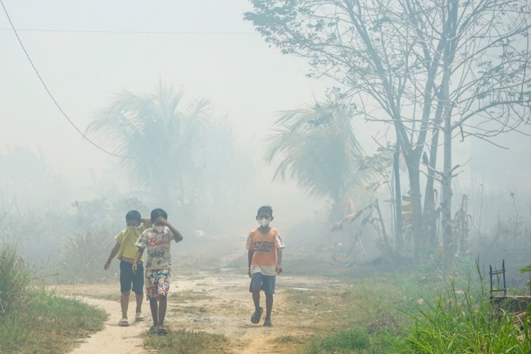 Children wearing face masks walk along a smoke-covered dirt road from the land and forest fire in Banjarbaru, South Kalimantan, on October 21, 2026. 