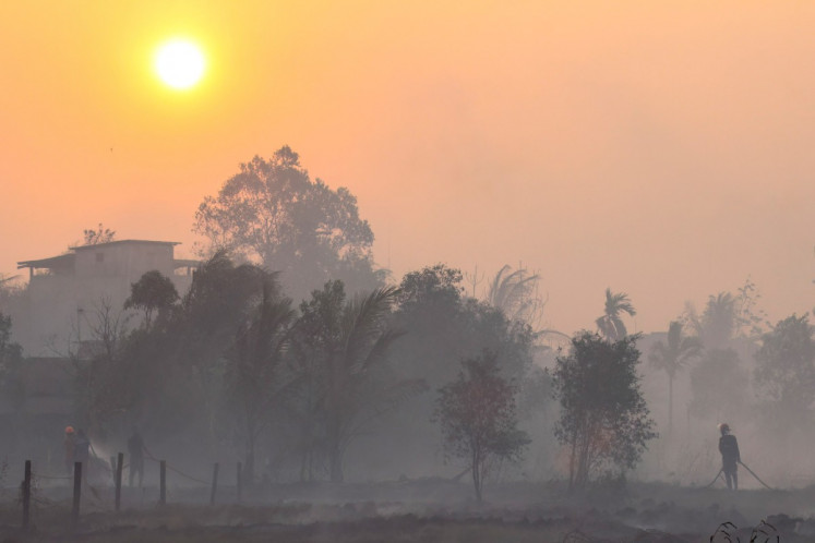 Firefighters and residents use hoses to extinguish spreading wildfires amid dense smoke and a hazy sunset in Banjarbaru, South Kalimantan, on Oct. 21, 2026.