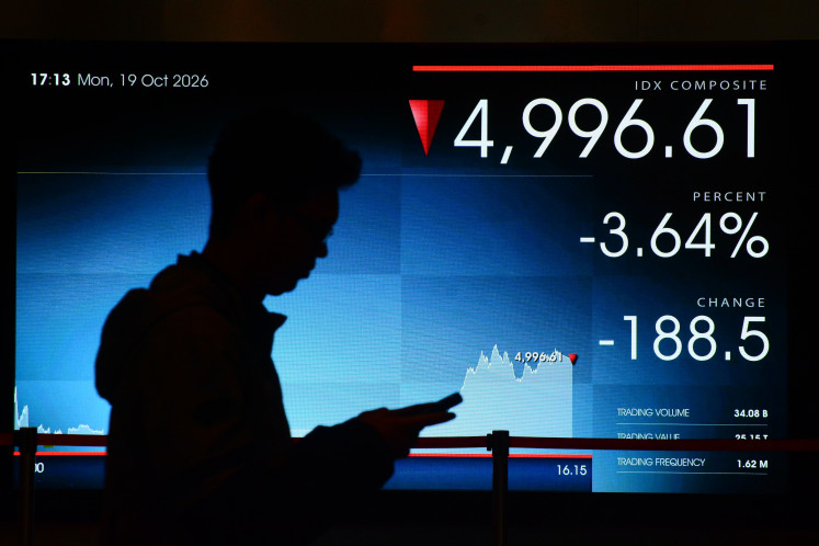 A visitor walks past a screen displaying the movement of the Jakarta Composite Index (JCI) on Oct. 19 at the Indonesia Stock Exchange in South Jakarta.
