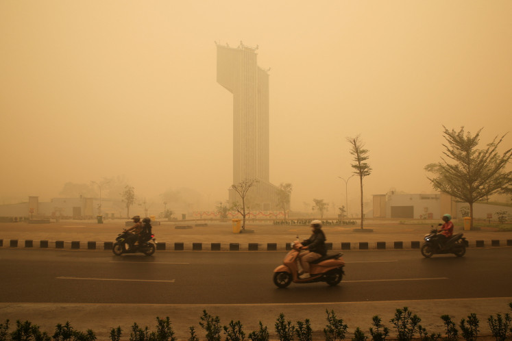 Motorcyclists wearing protective masks drive through the Talawang traffic circle as haze from wildfires shrouds the area in Palangka Raya, Central Kalimantan, on Oct. 24, 2026.