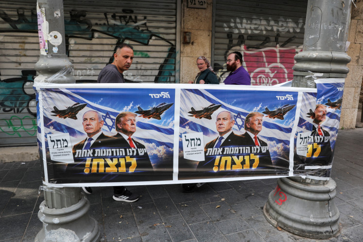 People walk past a poster of Israeli Prime Minister and Likud party leader Benjamin Netanyahu and US President Donald Trump during the country's national elections in central Jerusalem, October 27, 2026.